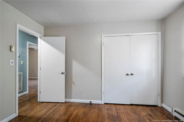 unfurnished bedroom featuring visible vents, a baseboard heating unit, baseboards, and wood finished floors