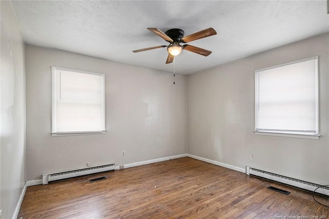 unfurnished room featuring ceiling fan, a baseboard heating unit, a healthy amount of sunlight, and wood finished floors