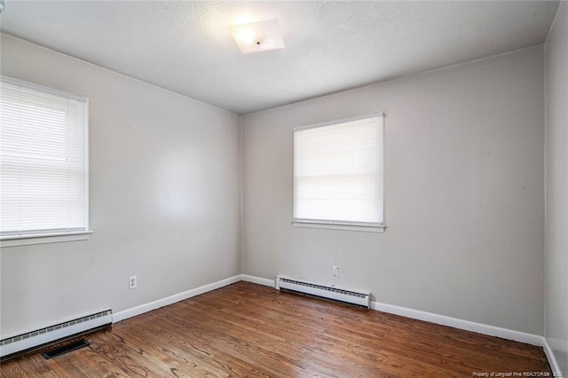 empty room featuring baseboards, baseboard heating, wood finished floors, and a textured ceiling