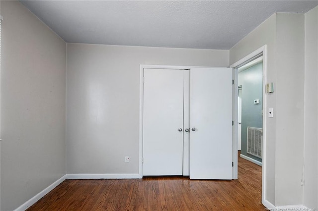 unfurnished bedroom featuring visible vents, a textured ceiling, wood finished floors, a closet, and baseboards