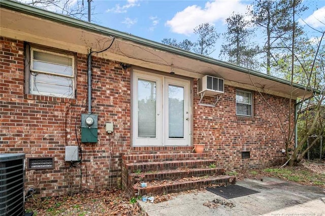 entrance to property with a wall mounted air conditioner, central air condition unit, and brick siding