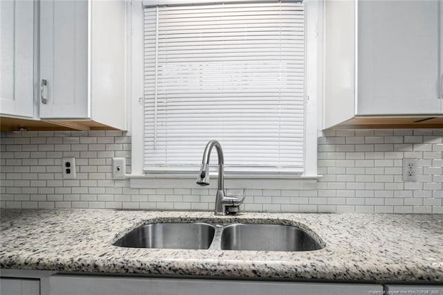 kitchen featuring white cabinets, a sink, backsplash, and light stone countertops