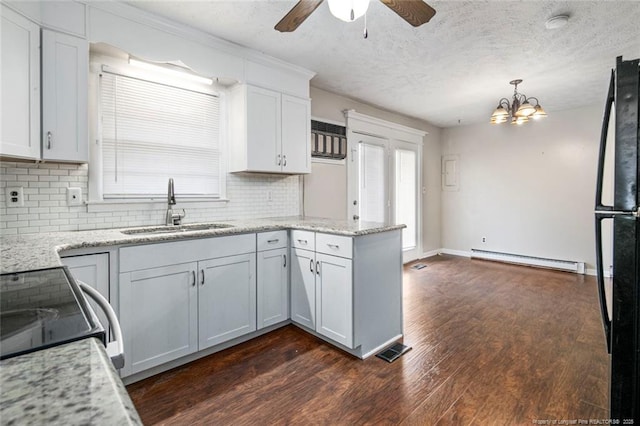 kitchen featuring a peninsula, baseboard heating, dark wood finished floors, a sink, and ceiling fan with notable chandelier