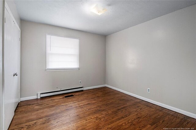 unfurnished room featuring a textured ceiling, visible vents, baseboards, wood finished floors, and a baseboard heating unit