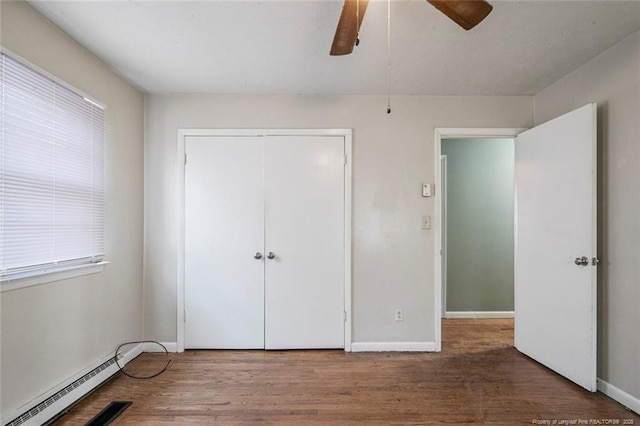 unfurnished bedroom with baseboard heating, baseboards, a ceiling fan, a closet, and wood finished floors