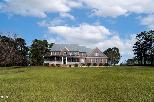 view of front of property featuring a chimney, brick siding, covered porch, and a front yard