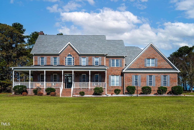 view of front of home with a porch, brick siding, a front lawn, and a chimney