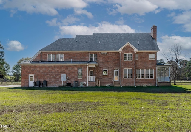 rear view of property with brick siding, entry steps, a chimney, and a yard