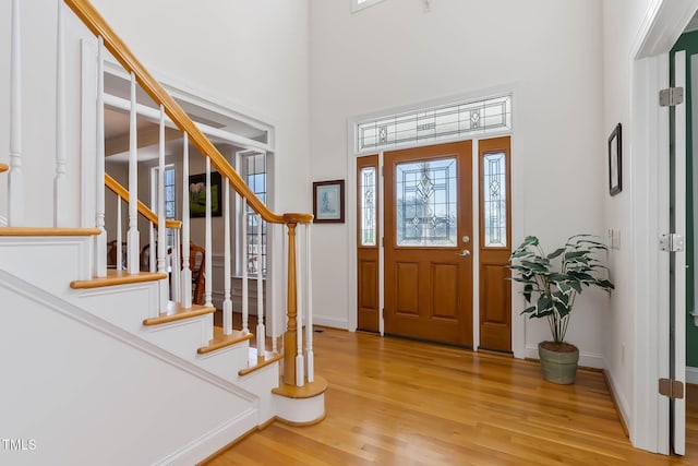 foyer featuring stairs, baseboards, light wood-type flooring, and a towering ceiling