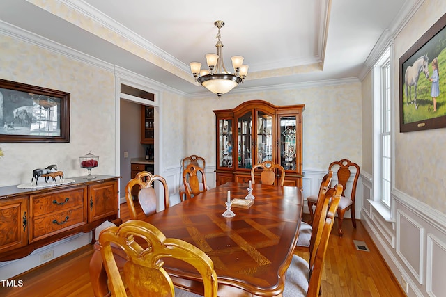 dining space with visible vents, a wainscoted wall, a notable chandelier, a tray ceiling, and light wood finished floors