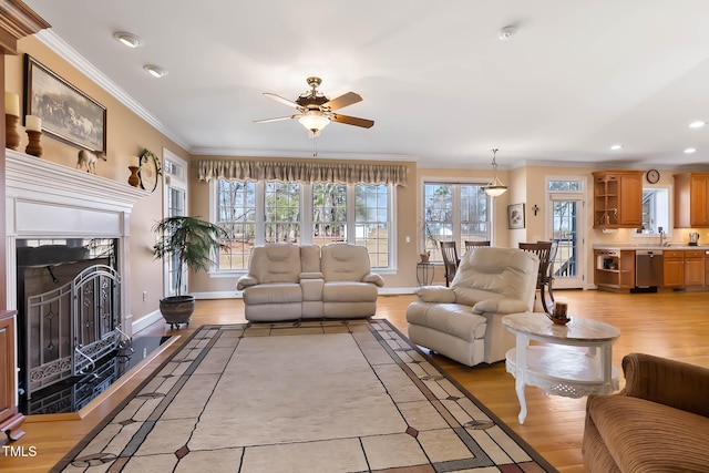 living room featuring a ceiling fan, baseboards, a fireplace, crown molding, and light wood-type flooring