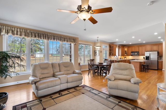 living area with light wood-style floors, baseboards, crown molding, and ceiling fan