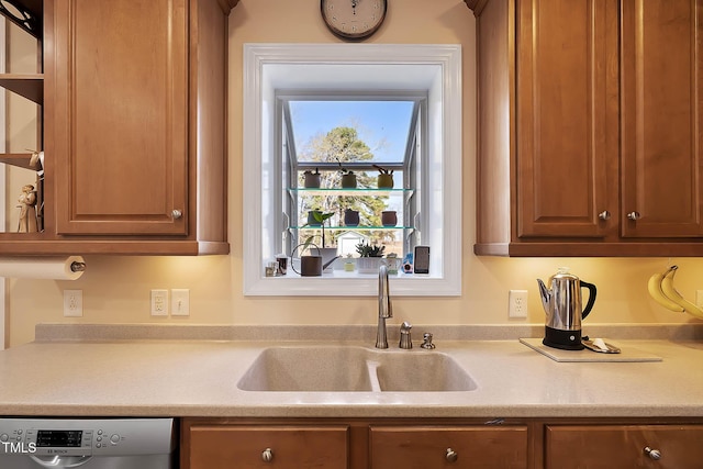 kitchen featuring dishwashing machine, brown cabinets, light countertops, and a sink