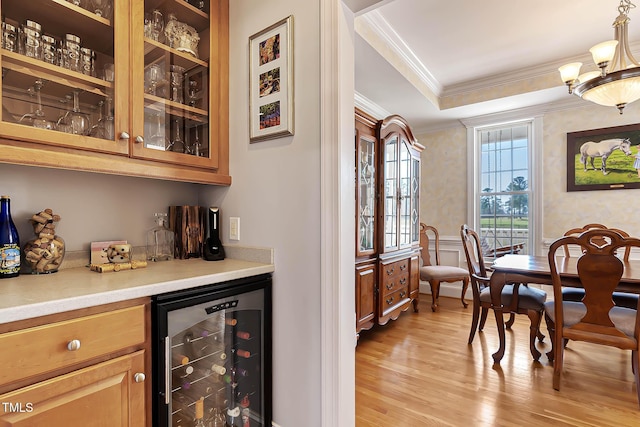 bar featuring crown molding, wine cooler, a wainscoted wall, light wood-style floors, and a bar