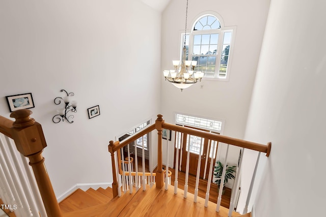 staircase with baseboards, wood finished floors, and a chandelier