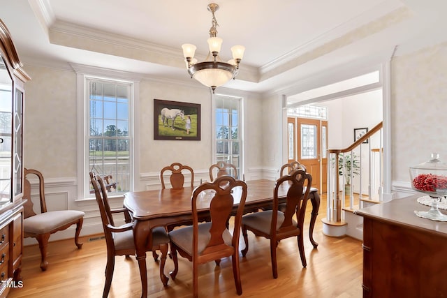 dining area featuring a wainscoted wall, a raised ceiling, and light wood-style floors