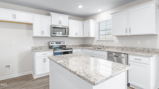 kitchen featuring light wood-type flooring, a sink, white cabinetry, appliances with stainless steel finishes, and baseboards