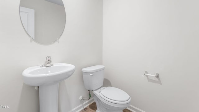 half bath with toilet, baseboards, and wood finished floors