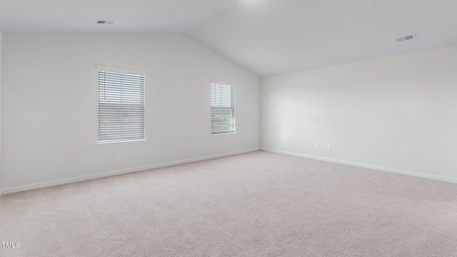 empty room featuring visible vents, lofted ceiling, light colored carpet, and baseboards