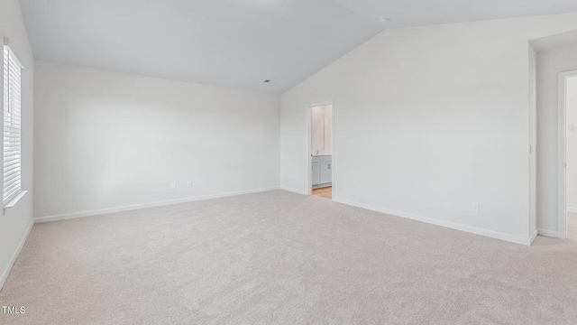 empty room featuring lofted ceiling, baseboards, and light carpet