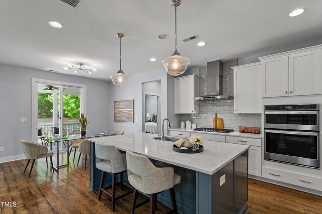 kitchen with visible vents, decorative backsplash, wall chimney exhaust hood, white cabinetry, and a sink