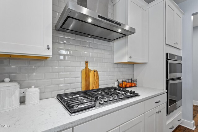 kitchen featuring wall chimney range hood, white cabinets, appliances with stainless steel finishes, and tasteful backsplash