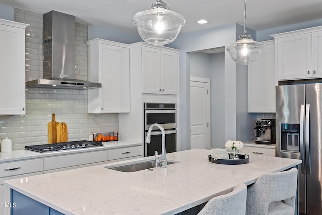kitchen featuring wall chimney range hood, white cabinets, appliances with stainless steel finishes, a sink, and a kitchen breakfast bar
