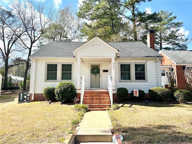 bungalow featuring a chimney, a front yard, and a shingled roof