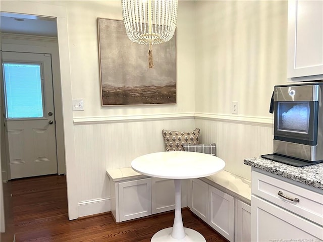 dining space featuring dark wood-style floors, a wainscoted wall, and a chandelier