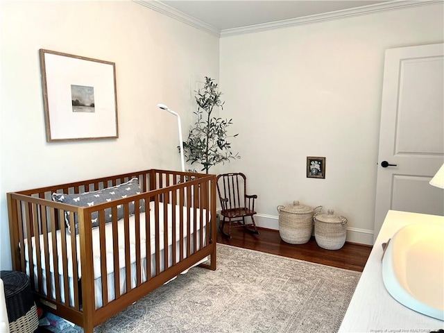 bedroom featuring ornamental molding, a sink, wood finished floors, a nursery area, and baseboards