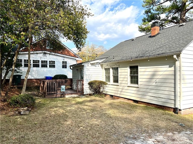 back of property with a chimney, a wooden deck, a yard, and a shingled roof