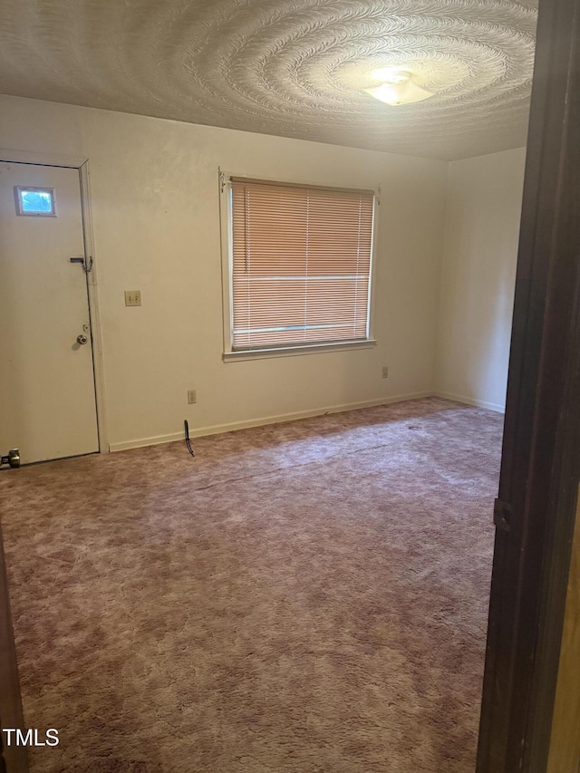 carpeted spare room featuring a textured ceiling and baseboards