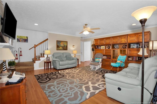 living room with stairway, wood finished floors, a ceiling fan, and crown molding