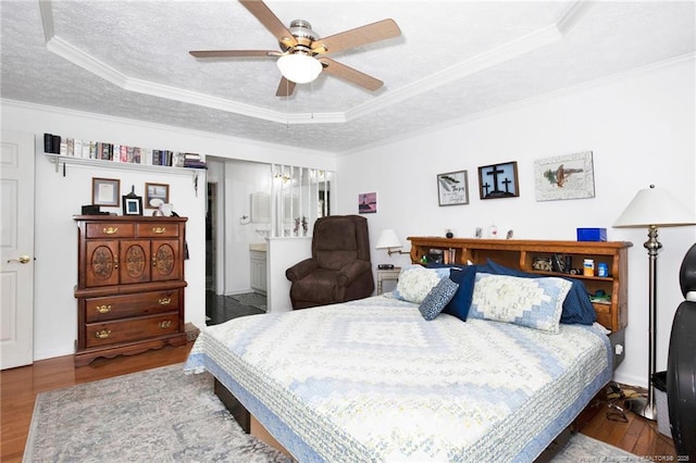 bedroom with ornamental molding, a tray ceiling, a textured ceiling, wood finished floors, and connected bathroom