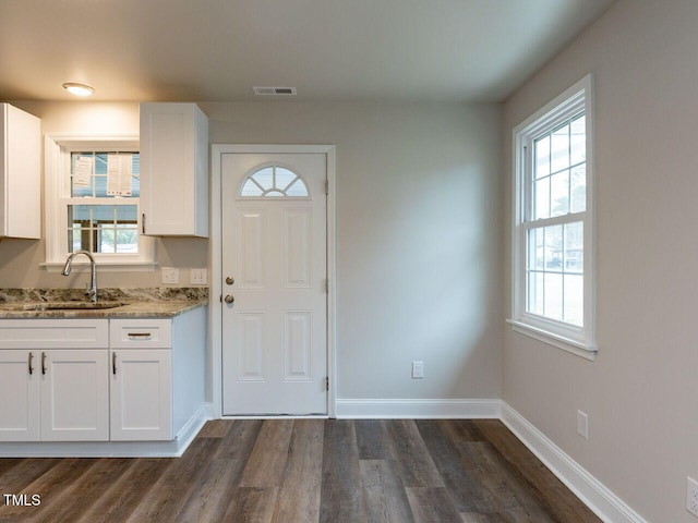 kitchen featuring a sink, light stone countertops, dark wood-type flooring, white cabinetry, and baseboards