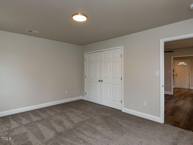 unfurnished bedroom with dark carpet, baseboards, and a closet