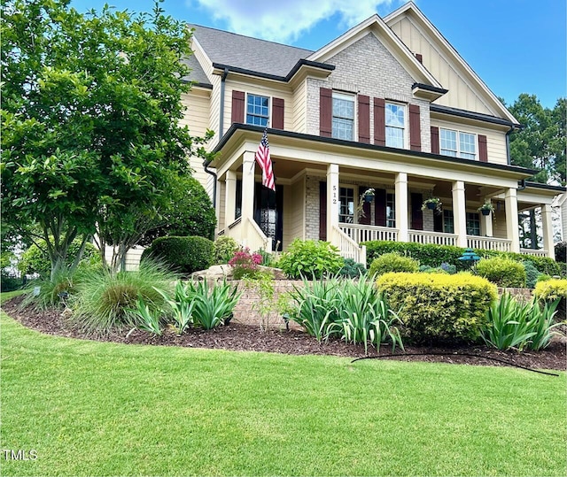 view of front of home featuring board and batten siding, a front lawn, covered porch, and brick siding