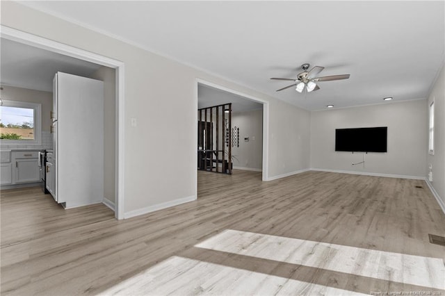 unfurnished living room with ornamental molding, a ceiling fan, light wood-style floors, and baseboards