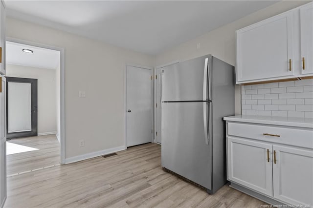 kitchen featuring visible vents, tasteful backsplash, freestanding refrigerator, light wood finished floors, and light countertops