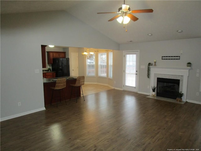 living area featuring a high end fireplace, baseboards, vaulted ceiling, ceiling fan with notable chandelier, and dark wood-style flooring