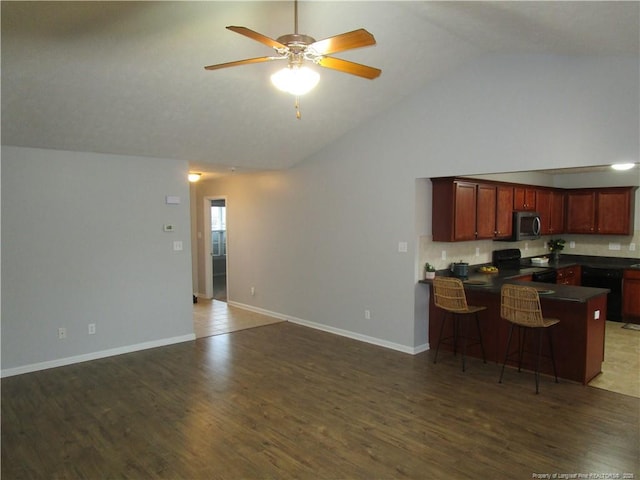 kitchen with a breakfast bar area, wood finished floors, a peninsula, black appliances, and dark countertops