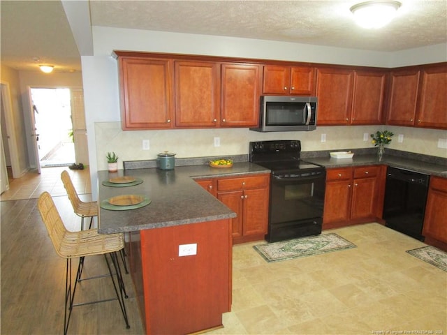 kitchen featuring dark countertops, a breakfast bar area, a peninsula, a textured ceiling, and black appliances