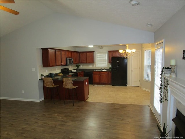 kitchen with black appliances, light wood-style flooring, a sink, dark countertops, and a peninsula