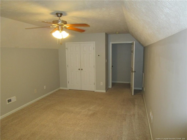 additional living space featuring a textured ceiling, baseboards, light colored carpet, ceiling fan, and vaulted ceiling