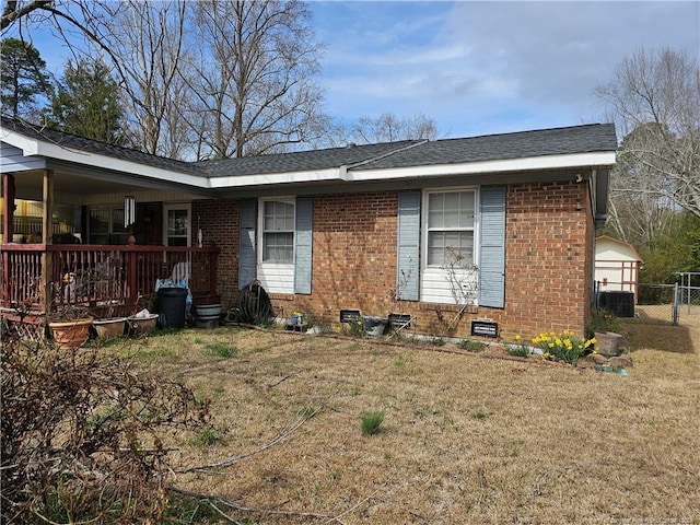 rear view of house featuring brick siding, a lawn, central AC, and roof with shingles