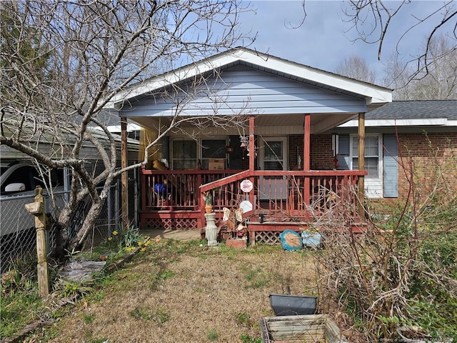 rear view of house with brick siding, a porch, and fence