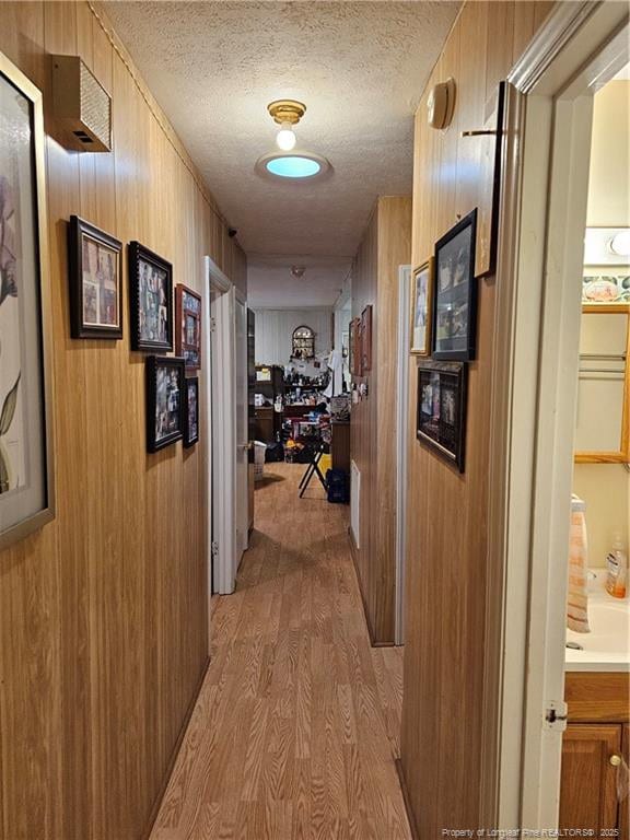 hall with wooden walls, light wood-style flooring, and a textured ceiling