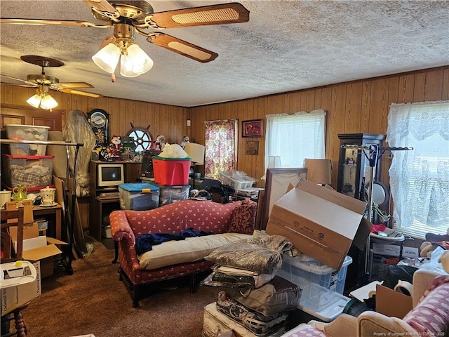 carpeted living room featuring wooden walls, a textured ceiling, a healthy amount of sunlight, and a ceiling fan