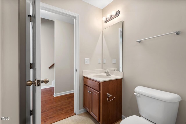half bathroom with vanity, baseboards, toilet, and wood finished floors