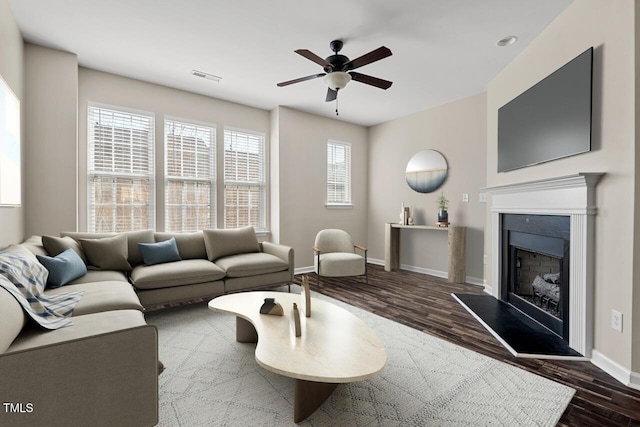living room with ceiling fan, visible vents, wood finished floors, baseboards, and a fireplace with raised hearth